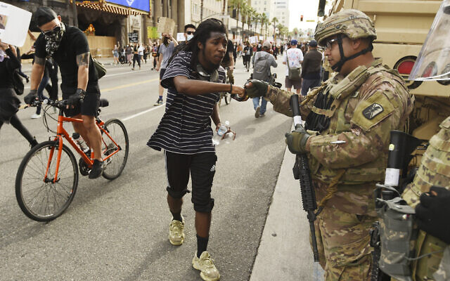 A protest rally participant bumps fists with a National Guardsman on Hollywood Boulevard, Tuesday, June 2, 2020, in Los Angeles. Protests were held in US cities over the death of George Floyd, a black man who died after being restrained by Minneapolis police officers on May 25. (AP Photo/Chris Pizzello)