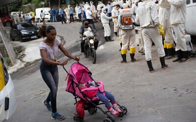 A woman pushing a baby stroller walks past water utility workers from CEDAE who will disinfect the Turano favela in an effort to curb the spread of the new coronavirus in Rio de Janeiro, June 9, 2020. (AP Photo/Silvia Izquierdo)