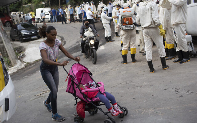 A woman pushing a baby stroller walks past water utility workers from CEDAE who will disinfect the Turano favela in an effort to curb the spread of the new coronavirus in Rio de Janeiro, June 9, 2020. (AP Photo/Silvia Izquierdo) A woman pushing a baby stroller walks past water utility workers from CEDAE who will disinfect the Turano favela in an effort to curb the spread of the new coronavirus in Rio de Janeiro, June 9, 2020. (AP Photo/Silvia Izquierdo)