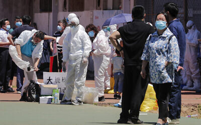 Workers put on protective suits as they wait for people living surrounding the Xinfadi wholesale market arrive to get a nucleic acid test at a stadium in Beijing, June 14, 2020. (AP Photo/Andy Wong)
