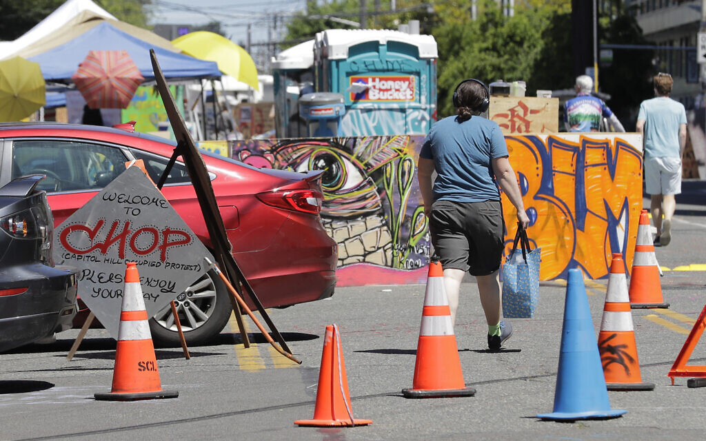 A person walks past a sign welcoming visitors Monday, June 22, 2020, near an entrance to what has been named the Capitol Hill Occupied Protest zone in Seattle. (AP Photo/Ted S. Warren)