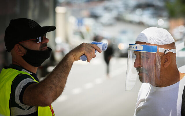 A man checks the temperature of a customer at the entrance to the market in the northern Israeli city of Tzfat, on June 3, 2020. (David Cohen/Flash90)