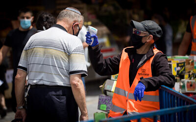 A man checks the temperature of a customer at the entrance to the Mahane Yehuda Market in Jerusalem on June 18, 2020. (Yonatan Sindel/Flash90)