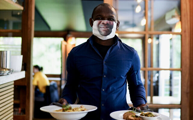 A waiter wearing a protective face mask with a picture of his face, works at the "Lodge" restaurant in Brussels, Belgium, June 8, 2020. (Kenzo Tribouillard/AFP) A waiter wearing a protective face mask with a picture of his face, works at the "Lodge" restaurant in Brussels, Belgium, June 8, 2020. (Kenzo Tribouillard/AFP)