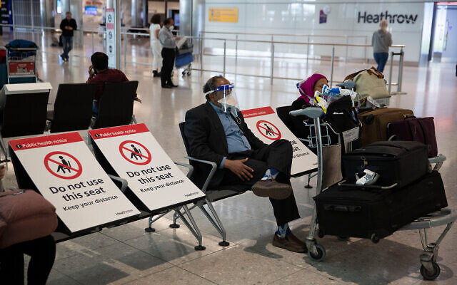A man sits wearing a face shield in the arrivals area on the first day of new rules mandating arrivals to Britain to quarantine themselves for 14 days to help stop the spread of coronavirus, at Heathrow Airpot in London, June 8, 2020. (AP/Matt Dunham) A man sits wearing a face shield in the arrivals area on the first day of new rules mandating arrivals to Britain to quarantine themselves for 14 days to help stop the spread of coronavirus, at Heathrow Airpot in London, June 8, 2020. (AP/Matt Dunham)