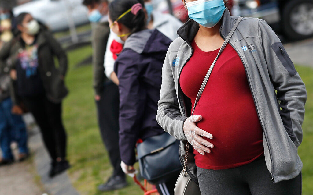 A pregnant woman wearing a face mask and gloves holds her belly as she waits in line for groceries in Waltham, Massachusetts, May 7, 2020. (AP Photo/Charles Krupa) A pregnant woman wearing a face mask and gloves holds her belly as she waits in line for groceries in Waltham, Massachusetts, May 7, 2020. (AP Photo/Charles Krupa)