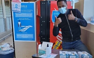 An employee at the entrance of an IGA grocery store in Cote Saint-Luc wears a mask near a station equipped with safety instructions, gloves, and hand sanitizer. (Courtesy)