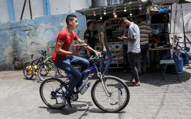A delivery employee carries a tray of steaming cups of coffee in front of Shaaban Hamuda's small stand near Rafah market, in the southern Gaza Strip, on July 13, 2020. (SAID KHATIB / AFP) A delivery employee carries a tray of steaming cups of coffee in front of Shaaban Hamuda's small stand near Rafah market, in the southern Gaza Strip, on July 13, 2020. (SAID KHATIB / AFP)