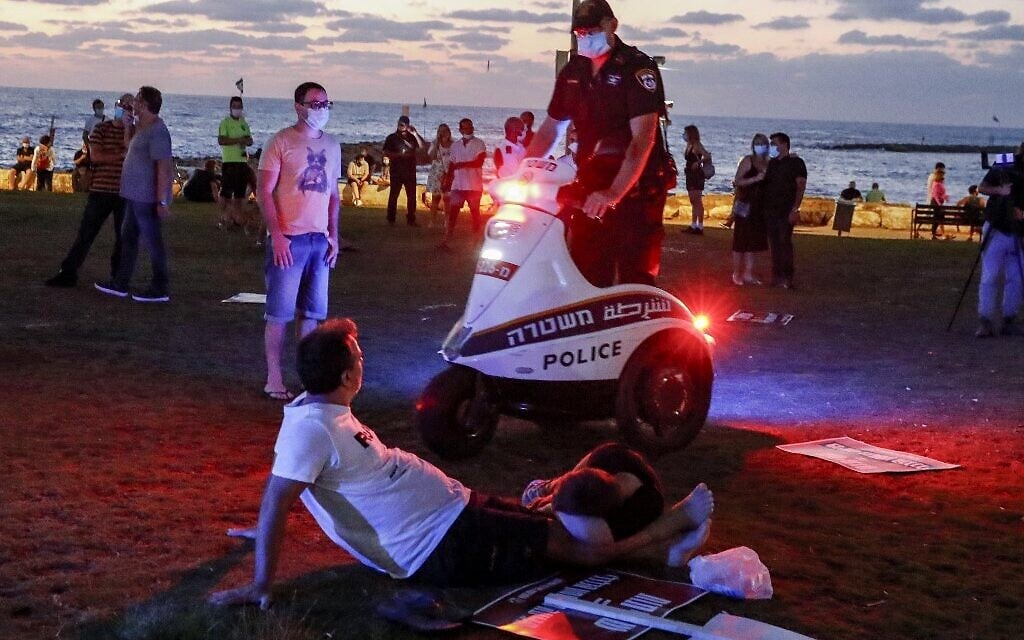 An Israeli policeman speaks with protesters from atop a scooter during a demonstration in Charles Clore Park in the Mediterranean coastal city of Tel Aviv on July 18, 2020 (Jack GUEZ / AFP)