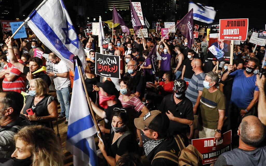Anti-government protesters, clad in masks due to the COVID-19 coronavirus pandemic, gather with Israeli flags and signs during a demonstration in Charles Clore Park in the Mediterranean coastal city of Tel Aviv on July 18, 2020 (Jack GUEZ / AFP)