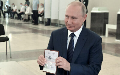 Russian President Vladimir Putin shows his passport to a member of an election commission as he arrives to take part in voting at a polling station in Moscow, Russia, July 1, 2020. (Alexei Druzhinin, Sputnik, Kremlin Pool Photo via AP)