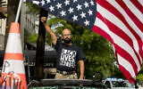 In this June 19, 2020, file photo, George Floyd's name is written on the windshield as John Coy wears a shirt that reads Black Lives Matter and stands through his sunroof with his fist in the air at 16th Street Northwest renamed Black Lives Matter Plaza near the White House in Washington.  (AP Photo/Andrew Harnik)
