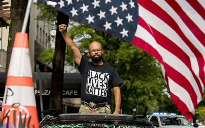 In this June 19, 2020, file photo, George Floyd's name is written on the windshield as John Coy wears a shirt that reads Black Lives Matter and stands through his sunroof with his fist in the air at 16th Street Northwest renamed Black Lives Matter Plaza near the White House in Washington.  (AP Photo/Andrew Harnik)