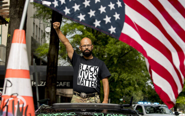 In this June 19, 2020, file photo, George Floyd's name is written on the windshield as John Coy wears a shirt that reads Black Lives Matter and stands through his sunroof with his fist in the air at 16th Street Northwest renamed Black Lives Matter Plaza near the White House in Washington. (AP Photo/Andrew Harnik) In this June 19, 2020, file photo, George Floyd's name is written on the windshield as John Coy wears a shirt that reads Black Lives Matter and stands through his sunroof with his fist in the air at 16th Street Northwest renamed Black Lives Matter Plaza near the White House in Washington. (AP Photo/Andrew Harnik)