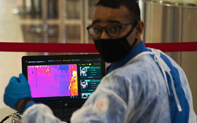 In this June 10, 2020, photo, an official wearing a mask due to the coronavirus pandemic operates a temperature screening point at Dubai International Airport's Terminal 3 in Dubai, United Arab Emirates. (AP Photo/Jon Gambrell)