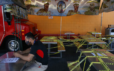 In this July 1, 2020, file photo, Abel Gomez waits for his order at Mariscos Linda food truck as dining tables are sealed off with caution tape due to the coronavirus pandemic in Los Angeles. (AP Photo/Jae C. Hong, File)