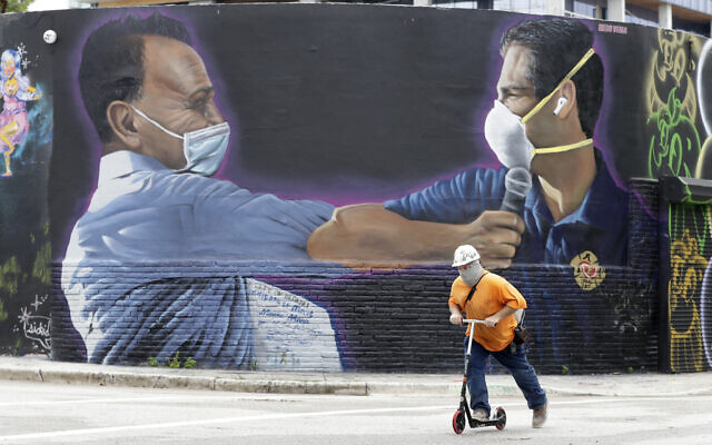 A construction worker rides a scooter past a mural by Hiero Veiga of billionaire businessman Moishe Mana, left, and City of Miami Mayor Francis X. Suarez wearing masks, July 13, 2020, in the Wynwood Arts District of Miami. (AP Photo/Wilfredo Lee) A construction worker rides a scooter past a mural by Hiero Veiga of billionaire businessman Moishe Mana, left, and City of Miami Mayor Francis X. Suarez wearing masks, July 13, 2020, in the Wynwood Arts District of Miami. (AP Photo/Wilfredo Lee)