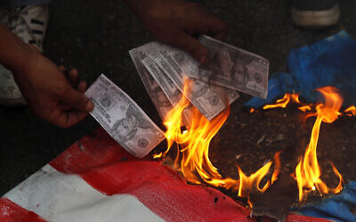 A supporter of a communist group burns representation of US currency, during a protest against US interference in Lebanon's affairs, near the US embassy, in Aukar northeast of Beirut, Lebanon,  July 10, 2020. (Hussein Malla/AP)