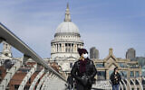 People wear masks as they walk in London over the River Thames on Millennium Bridge near St Paul's Cathedral, seen in the background, March 22, 2020. (AP Photo/Kirsty Wigglesworth)