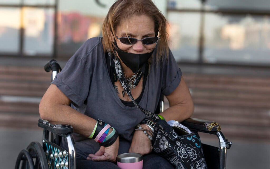 In this Thursday, May 14, 2020 photo, homeless person Candice Moore waits to catch a bus back to her hotel before her curfew in Los Angeles. (AP Photo/Damian Dovarganes)
