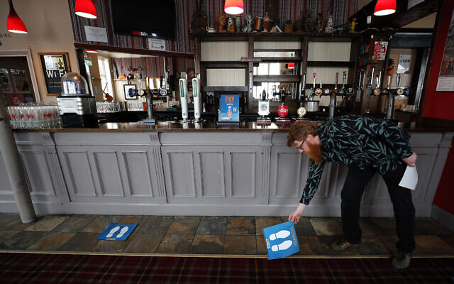 Owner Are Kjetil Kolltveit places markers for social distancing on the front of the bar at the Chandos Arms pub in London, July 1, 2020 (AP Photo/Frank Augstein) Owner Are Kjetil Kolltveit places markers for social distancing on the front of the bar at the Chandos Arms pub in London, July 1, 2020 (AP Photo/Frank Augstein)