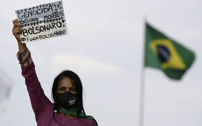 A women's movement activist holds a sign that reads in Portuguese 'Genocide 60 thousand deaths, Bolsonaro out,' during a protest against the government's inefficiency in the face of the new coronavirus pandemic and the ongoing police brutality against blacks, in front of the National Congress, in Brasilia, Brazil, July 2, 2020. (AP Photo/Eraldo Peres)