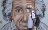 An Israeli man wearing a mask to curb the spread of the coronavirus walks past a mural showing Albert Einstein in Tel Aviv, July 15, 2020. (AP/Sebastian Scheiner)