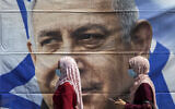 Muslim women wearing face masks walk past a poster hung by supporters of Prime Minister Benjamin Netanyahu outside the District Court in Jerusalem, July 19, 2020 (AP Photo/Ariel Schalit)