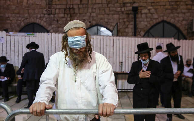 A man uses a mask as a blindfold at the burial site of Rabbi Shimon bar Yohai in Mount Meron on July 7, 2020. (David Cohen/Flash90) A man uses a mask as a blindfold at the burial site of Rabbi Shimon bar Yohai in Mount Meron on July 7, 2020. (David Cohen/Flash90)