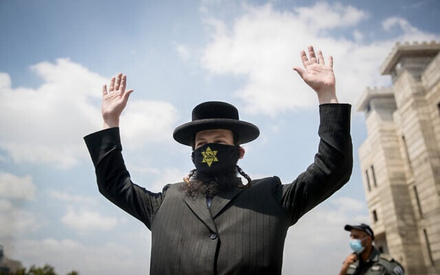 An ultra-Orthodox Jewish man wears a face mask with a yellow star on and raises his hands at a roadblock in the Hephzibah neighborhood in Beit Shemesh that is currently under a lock down in an attempt to prevent the spread of the Coronavirus, on July 10, 2020. (Yonatan Sindel/Flash90) An ultra-Orthodox Jewish man wears a face mask with a yellow star on and raises his hands at a roadblock in the Hephzibah neighborhood in Beit Shemesh that is currently under a lock down in an attempt to prevent the spread of the Coronavirus, on July 10, 2020. (Yonatan Sindel/Flash90)