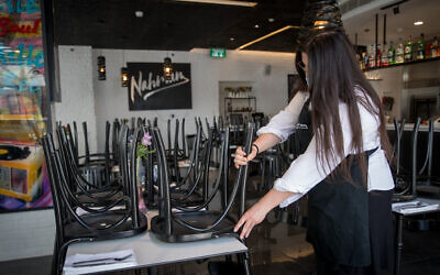 A waitress handles chairs in a restaurant in downtown Jerusalem on July 17, 2020. (Yonatan Sindel/Flash90)