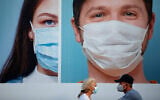 People wearing protective face masks pass a billboard in Ramat Gan, near Tel Aviv, July 16, 2020. (AP Photo/Oded Balilty)
