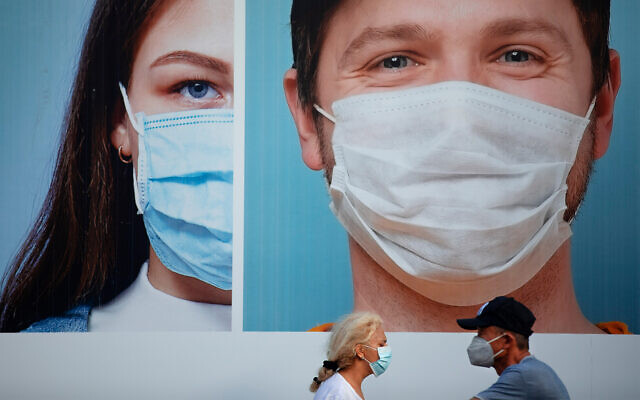 People wearing protective face masks pass a billboard in Ramat Gan, near Tel Aviv, July 16, 2020. (AP Photo/Oded Balilty) People wearing protective face masks pass a billboard in Ramat Gan, near Tel Aviv, July 16, 2020. (AP Photo/Oded Balilty)