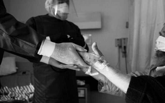 A volunteer visitor who recovered from COVID-19 holds the hand of a patient on a coronavirus ward at Hadassah University Hospital in Ein Kerem, as a hospital employee looks on. (Eli Atias) A volunteer visitor who recovered from COVID-19 holds the hand of a patient on a coronavirus ward at Hadassah University Hospital in Ein Kerem, as a hospital employee looks on. (Eli Atias)