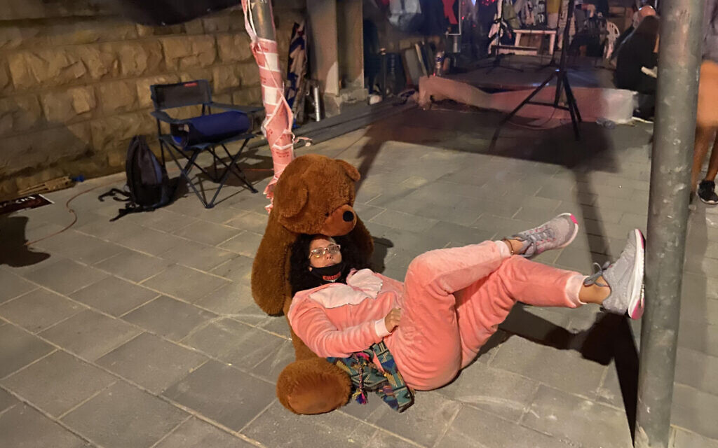 Mirav Ben-Uziel, in her pink pajama onesies and with her teddy bear, outside the Prime Minister's Residence in Jerusalem, July 16, 2020 (Anat Peled)