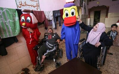 Disabled Gazan couple Nihad Jarboa, 37, (L) and his wife Zeinab, 35, sit on their wheelchairs as clients try on cartoon-inspired costumes stitched by them, at their home in the Rafah refugee camp in the southern Gaza Strip, on July 19, 2020. (Photo by SAID KHATIB / AFP)