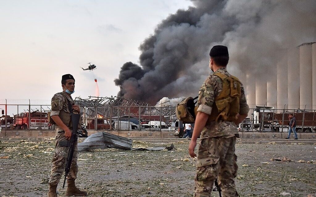Lebanese army soldiers stand while behind a helicopter puts out a fire at the scene of an explosion at the port of Lebanon's capital Beirut on August 4, 2020. (STR / AFP) Lebanese army soldiers stand while behind a helicopter puts out a fire at the scene of an explosion at the port of Lebanon's capital Beirut on August 4, 2020. (STR / AFP)