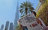 A man reads a copy of UAE-based The National newspaper, with a headline about the UAE-Israel agreement and Israel's suspension of annexation moves, near the Burj Khalifa, the tallest structure and building in the world, in Dubai on August 14, 2020. (Photo by Giuseppe Cacace/AFP)