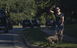 A resident walking her dog gestures as the motorcade of US President Donald Trump drives by towards the Trump National Golf Club in Sterling, Virginia, August 30, 2020. (AP Photo/Manuel Balce Ceneta)