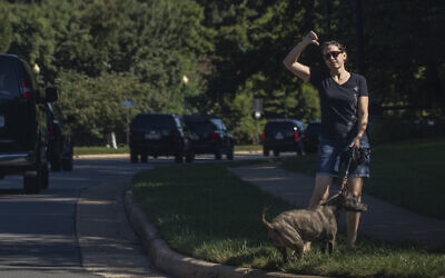 A resident walking her dog gestures as the motorcade of US President Donald Trump drives by towards the Trump National Golf Club in Sterling, Virginia, August 30, 2020. (AP Photo/Manuel Balce Ceneta)