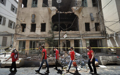 University students who volunteered to help clean damaged homes and give other assistance, pass in front of a building that was damaged by last week's explosion, in Beirut, Lebanon, Aug. 11, 2020 (AP Photo/Hussein Malla)