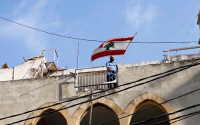 In this Friday, Aug. 7, 2020, file photo, a man puts a Lebanese flag on the roof of a damaged building at a neighborhood near the scene of an explosion that hit the seaport of Beirut, Lebanon (AP Photo/Thibault Camus, File)