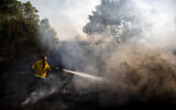 A firefighter attempts to extinguish a fire started by an incendiary device launched from the Gaza Strip, in Kibbutz Kfar Aza on the border with Gaza, August 24, 2020. (AP/Ariel Schalit)
