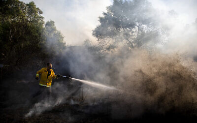 A firefighter attempts to extinguish a fire started by an incendiary device launched from the Gaza Strip, in Kibbutz Kfar Aza on the border with Gaza, August 24, 2020. (AP/Ariel Schalit)