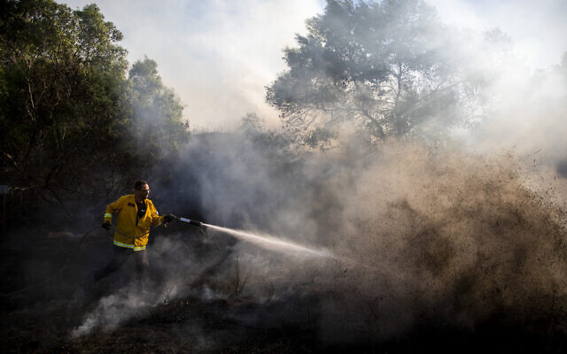 A firefighter attempts to extinguish a fire started by an incendiary device launched from the Gaza Strip, in Kibbutz Kfar Aza on the border with Gaza, August 24, 2020. (AP/Ariel Schalit) A firefighter attempts to extinguish a fire started by an incendiary device launched from the Gaza Strip, in Kibbutz Kfar Aza on the border with Gaza, August 24, 2020. (AP/Ariel Schalit)