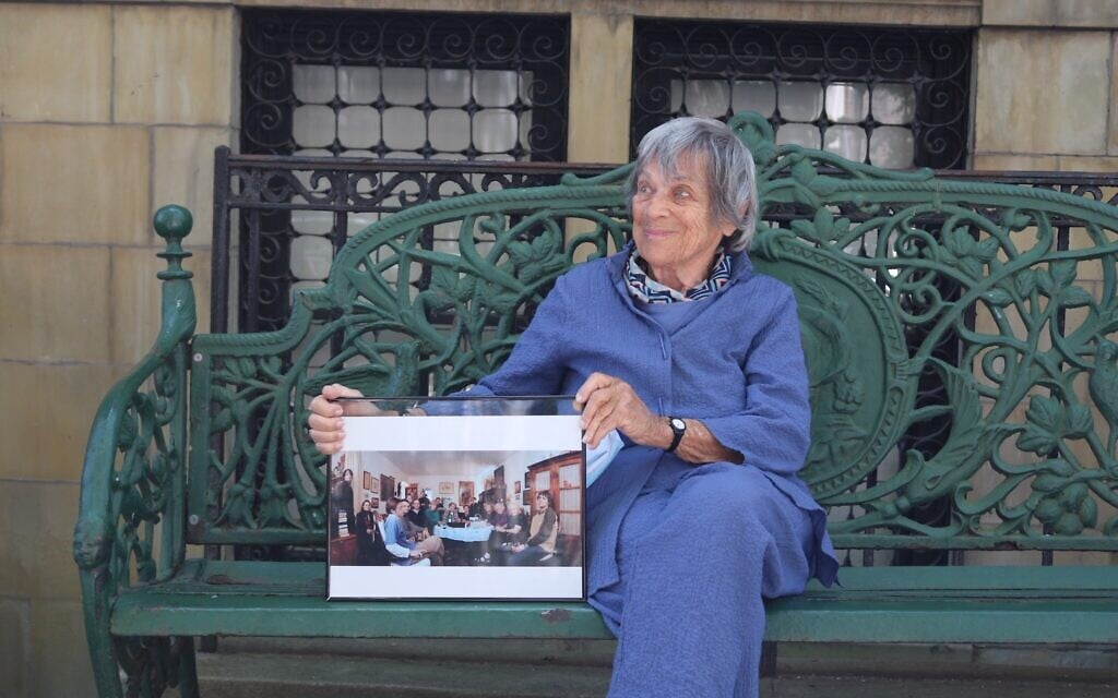 94-year-old Trudy Jeremias has taken over hosting the Stammtisch since 2015. Here, in 2020, she holds a photo of the regular Wednesday meeting at the home of her predecessor, Gaby Glueckselig. (Hannah Harnest/ Times of Israel)