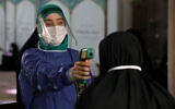 A volunteer wearing protective gear to help prevent the spread of the coronavirus checks temperature at a mosque in Tehran, July 30, 2020. (AP Photo/Vahid Salemi)