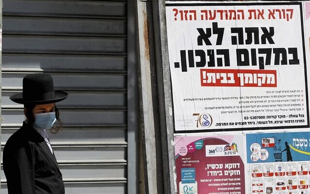 In this file photo taken on April 03, 2020 an ultra-Orthodox man wearing a mask walks past a sign reading in Hebrew 'Reading this ad? You're not in the right place. Your place is at home,' in the religious Israeli city of Bnei Brak, near Tel Aviv (JACK GUEZ / AFP) In this file photo taken on April 03, 2020 an ultra-Orthodox man wearing a mask walks past a sign reading in Hebrew 'Reading this ad? You're not in the right place. Your place is at home,' in the religious Israeli city of Bnei Brak, near Tel Aviv (JACK GUEZ / AFP)