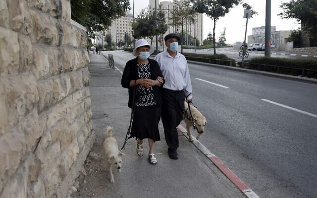 A mask-clad couple walk along a street in Jerusalem during the second nationwide lockdown imposed by the government in a bid to stem the spread of the coronavirus COVID-19, on September 26, 2020. (MENAHEM KAHANA / AFP)
