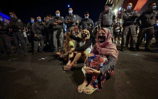 Protesters sit near policemen during a demonstration in front of Prime Minister Benjamin Netanyahu's residence in Jerusalem, on September 26, 2020, to protest the government's handling of the COVID-19 pandemic. Thousands of Israelis gathered in Jerusalem to demand the resignation of Netanyahu, a day after the country tightened its lockdown aimed at slowing coronavirus spread. (Emmanuel DUNAND / AFP) Protesters sit near policemen during a demonstration in front of Prime Minister Benjamin Netanyahu's residence in Jerusalem, on September 26, 2020, to protest the government's handling of the COVID-19 pandemic. Thousands of Israelis gathered in Jerusalem to demand the resignation of Netanyahu, a day after the country tightened its lockdown aimed at slowing coronavirus spread. (Emmanuel DUNAND / AFP)